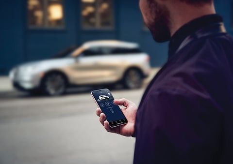 A person is shown interacting with a smartphone to connect to a Lincoln vehicle across the street. | Mark McLarty Lincoln in North Little Rock AR