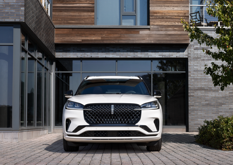A white 2025 Lincoln Aviator® SUV is shown parked outside a modern building with gray brick and wood accents. | Mark McLarty Lincoln in North Little Rock AR