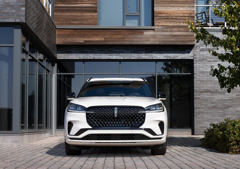 A white 2025 Lincoln Aviator® SUV is shown parked outside a modern building with gray brick and wood accents. | Mark McLarty Lincoln in North Little Rock AR