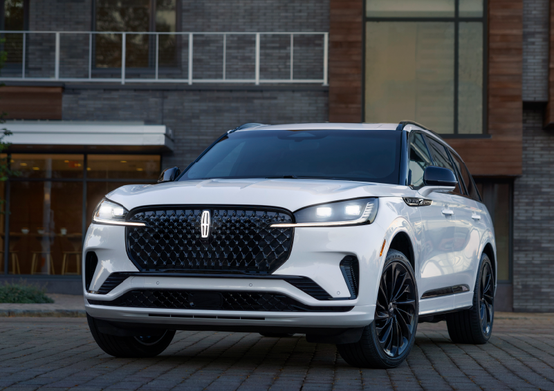 A white 2025 Lincoln Aviator® SUV is shown parked outside a modern building with gray brick and wood accents. | Mark McLarty Lincoln in North Little Rock AR