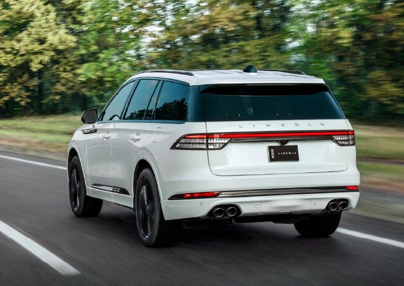 A white 2026 Lincoln Aviator® SUV is being driven away down a road lined with colorful trees. | Mark McLarty Lincoln in North Little Rock AR
