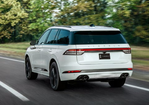 A white 2026 Lincoln Aviator® SUV is being driven away down a road lined with colorful trees. | Mark McLarty Lincoln in North Little Rock AR