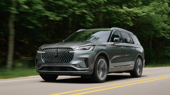 A 2027 Lincoln Aviator® SUV is being driven down a road lined with trees. | McLarty Lincoln in North Little Rock AR